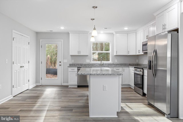 kitchen with white cabinetry, light stone counters, a kitchen island, pendant lighting, and stainless steel appliances