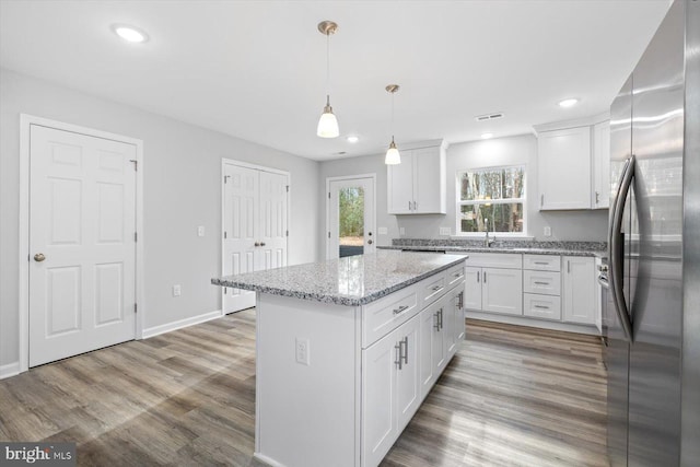 kitchen with stainless steel refrigerator, white cabinetry, hanging light fixtures, light stone counters, and a kitchen island