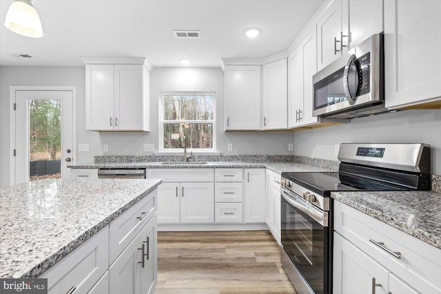 kitchen featuring decorative light fixtures, a wealth of natural light, stainless steel appliances, and white cabinets