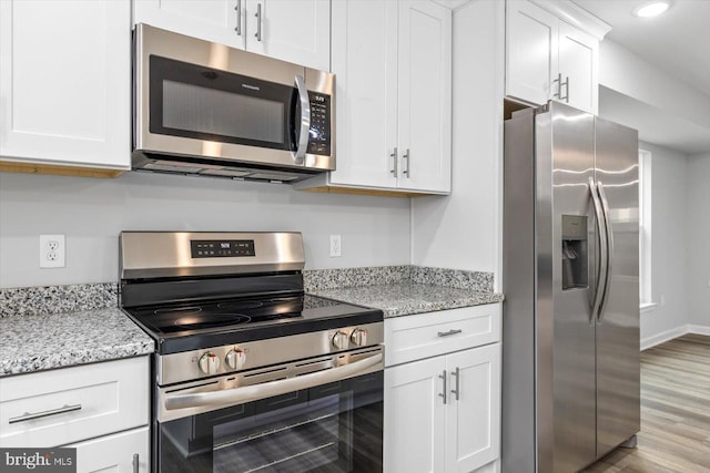 kitchen featuring stainless steel appliances, light stone countertops, light wood-type flooring, and white cabinets