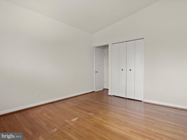 unfurnished bedroom featuring vaulted ceiling, a closet, and light wood-type flooring