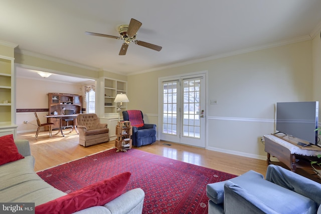 living area with baseboards, wood finished floors, a ceiling fan, and crown molding