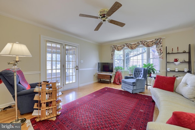 living area featuring a ceiling fan, baseboards, ornamental molding, and wood finished floors