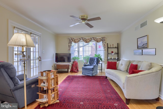 living area with a ceiling fan, crown molding, visible vents, and wood finished floors