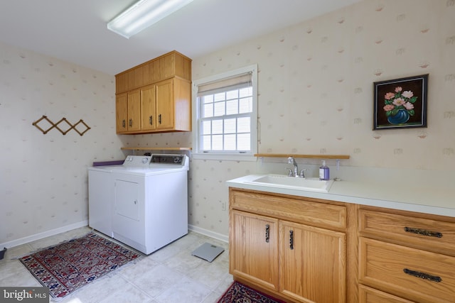 washroom with a sink, baseboards, cabinet space, washing machine and clothes dryer, and wallpapered walls