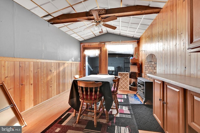 dining space featuring ceiling fan, wood walls, wood-type flooring, and vaulted ceiling