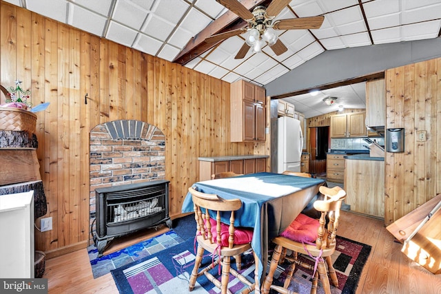 dining area with wood walls, lofted ceiling, a wood stove, ceiling fan, and wood-type flooring