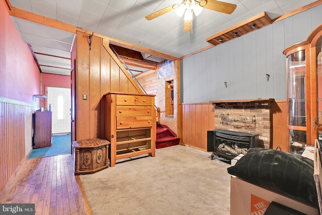 carpeted living room with a fireplace, ceiling fan, and wood walls