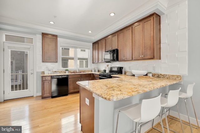 kitchen with light stone countertops, a kitchen bar, black appliances, and kitchen peninsula