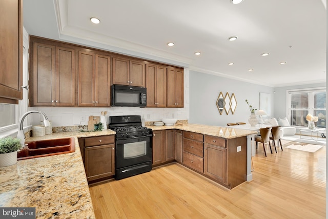 kitchen with sink, light stone counters, light hardwood / wood-style flooring, kitchen peninsula, and black appliances