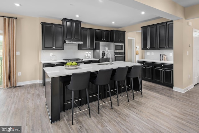 kitchen with appliances with stainless steel finishes, a breakfast bar, an island with sink, sink, and light hardwood / wood-style floors