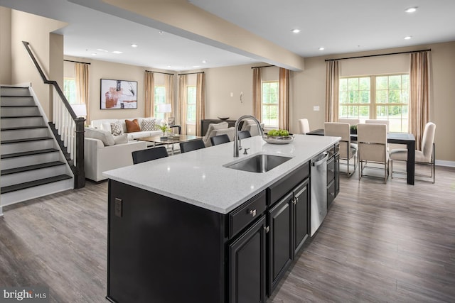 kitchen with sink, dishwasher, light stone countertops, a center island with sink, and light wood-type flooring