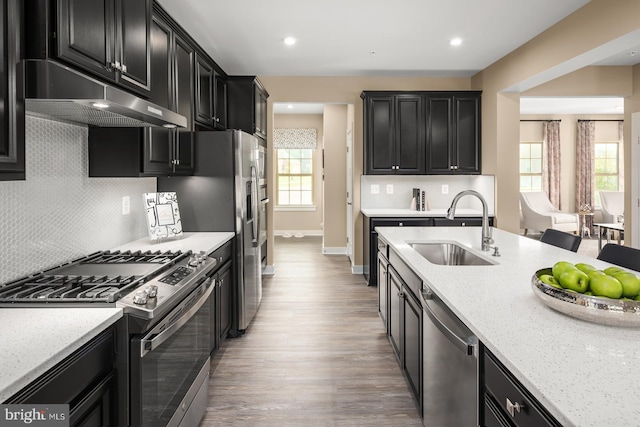 kitchen with sink, appliances with stainless steel finishes, tasteful backsplash, light stone countertops, and light wood-type flooring