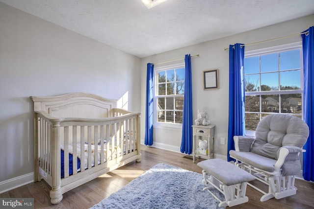 bedroom with a textured ceiling, a crib, wood-type flooring, and multiple windows