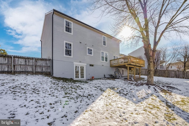 snow covered rear of property with french doors and a wooden deck