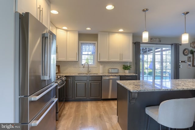 kitchen featuring stainless steel appliances, white cabinets, tasteful backsplash, light stone countertops, and pendant lighting