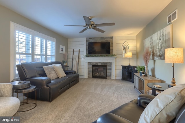 living room featuring ceiling fan, light colored carpet, a tiled fireplace, and wood walls