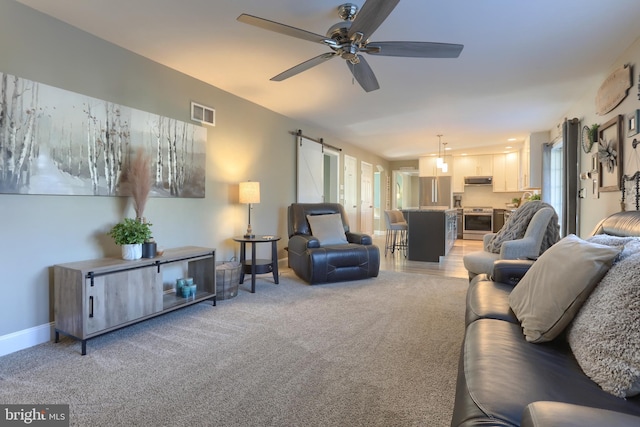 carpeted living room with ceiling fan and a barn door