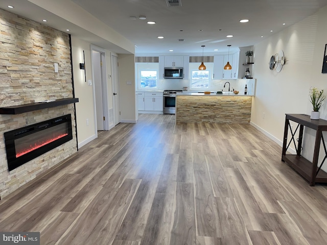 interior space featuring appliances with stainless steel finishes, decorative light fixtures, white cabinetry, a stone fireplace, and hardwood / wood-style flooring