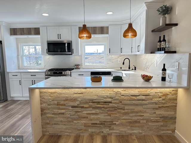 kitchen featuring white cabinetry, light hardwood / wood-style floors, appliances with stainless steel finishes, pendant lighting, and sink