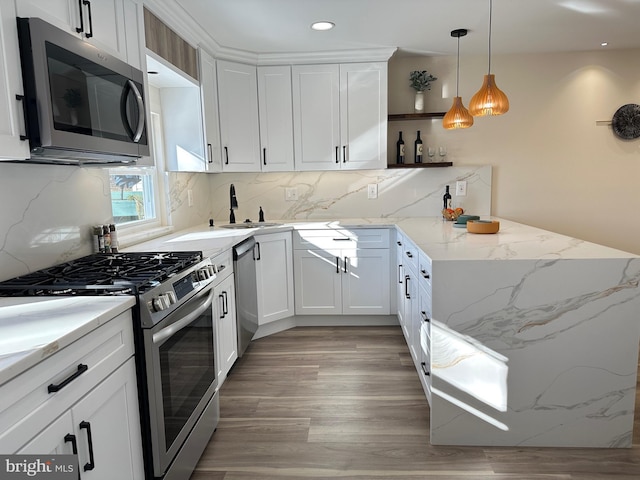 kitchen featuring light stone countertops, white cabinets, appliances with stainless steel finishes, sink, and hanging light fixtures