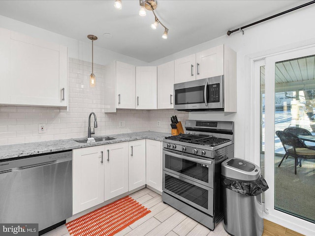 kitchen featuring light stone countertops, pendant lighting, appliances with stainless steel finishes, white cabinetry, and sink