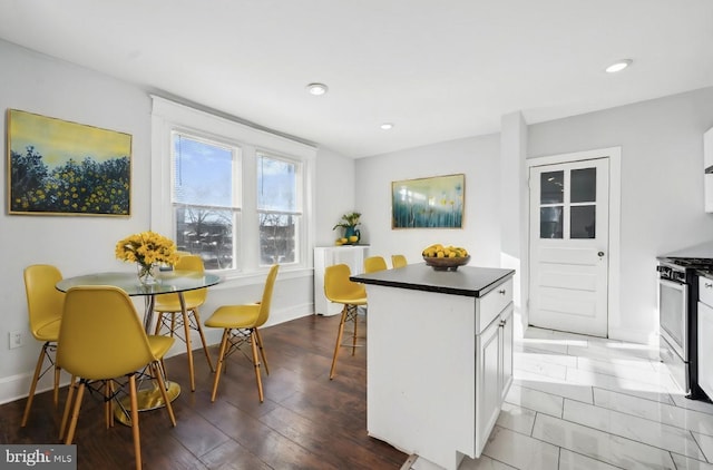 kitchen featuring a kitchen island, a kitchen bar, wood-type flooring, stainless steel gas range, and white cabinets