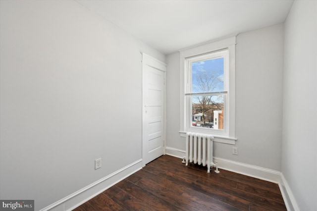 empty room with radiator heating unit and dark hardwood / wood-style flooring