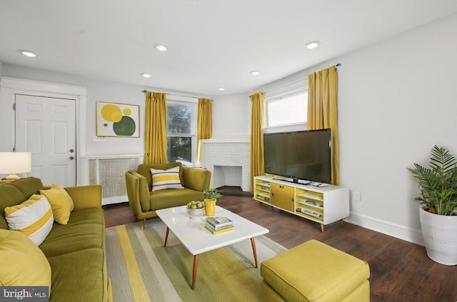 living room with a brick fireplace, dark hardwood / wood-style floors, and radiator heating unit