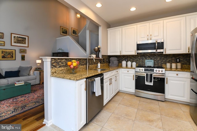 kitchen featuring white cabinets, stainless steel appliances, dark stone countertops, sink, and kitchen peninsula