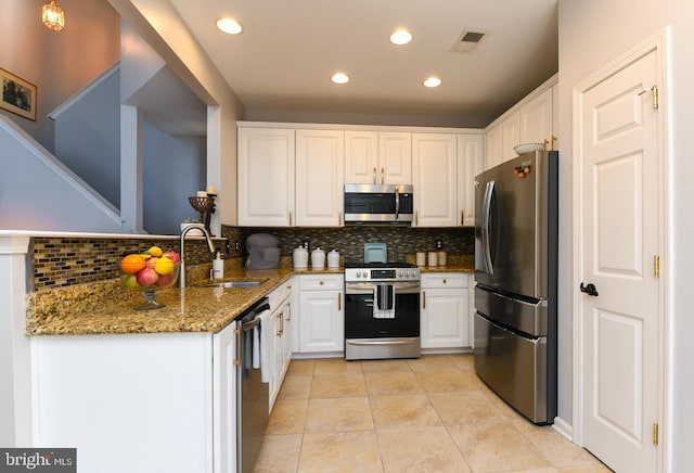 kitchen with kitchen peninsula, stainless steel appliances, stone counters, white cabinets, and sink