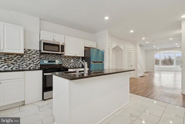 kitchen with white cabinetry, sink, decorative backsplash, a kitchen island with sink, and stainless steel appliances