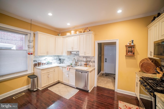 kitchen with tasteful backsplash, white cabinets, appliances with stainless steel finishes, ornamental molding, and sink