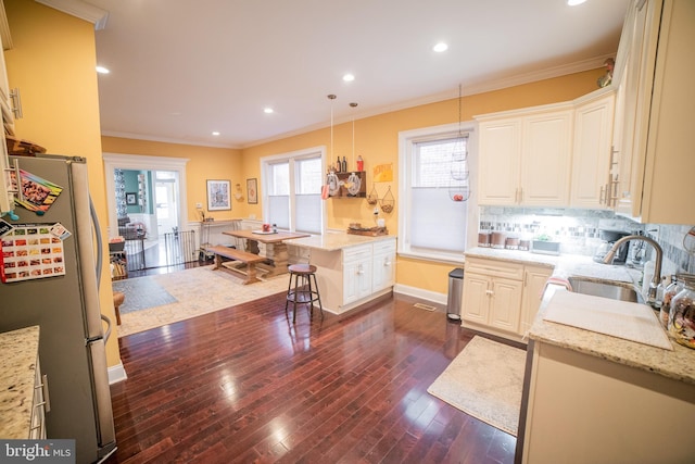 kitchen with light stone countertops, decorative light fixtures, a breakfast bar, stainless steel refrigerator, and ornamental molding