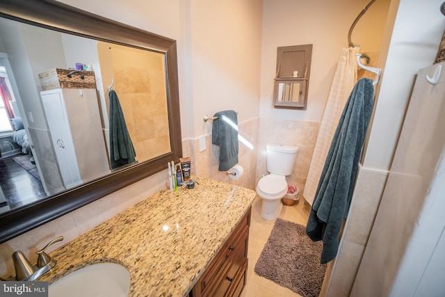 bathroom featuring toilet, walk in shower, tile patterned floors, vanity, and tile walls