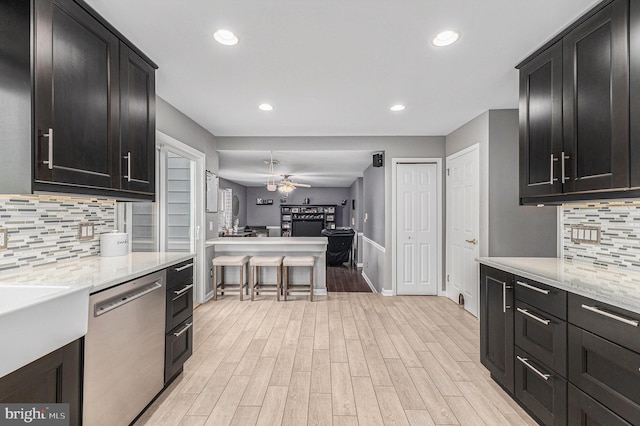 kitchen featuring tasteful backsplash, dishwasher, light stone counters, and light hardwood / wood-style flooring