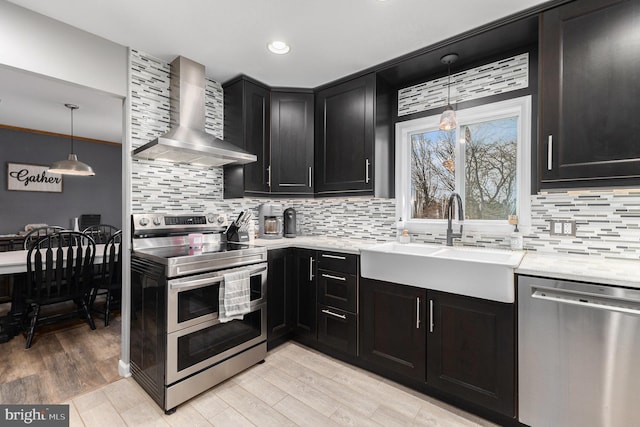 kitchen featuring appliances with stainless steel finishes, light wood-type flooring, hanging light fixtures, wall chimney range hood, and sink