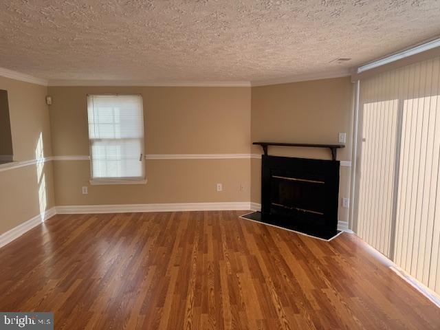 unfurnished living room with hardwood / wood-style floors, a textured ceiling, and ornamental molding