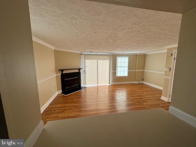 unfurnished living room featuring wood-type flooring, a textured ceiling, and ornamental molding