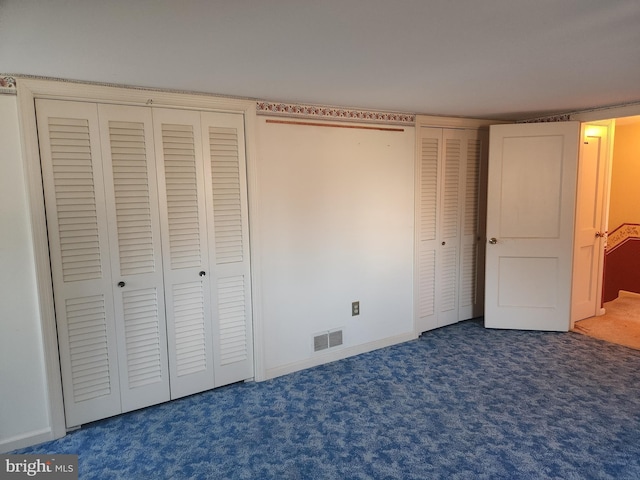 unfurnished bedroom with dark colored carpet and multiple closets