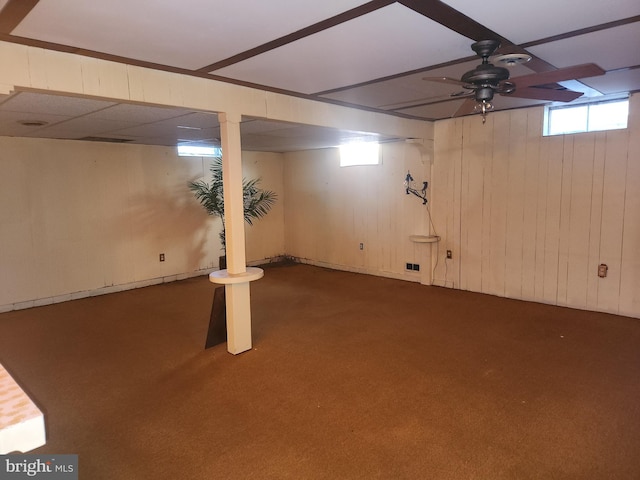 basement with wood walls, ceiling fan, and dark carpet