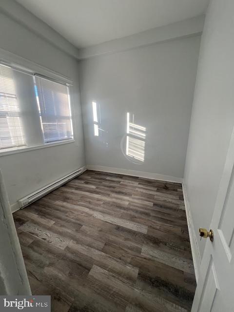 empty room featuring baseboard heating and dark hardwood / wood-style floors