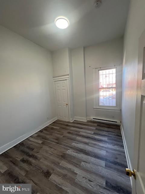 unfurnished room with baseboard heating and dark hardwood / wood-style flooring