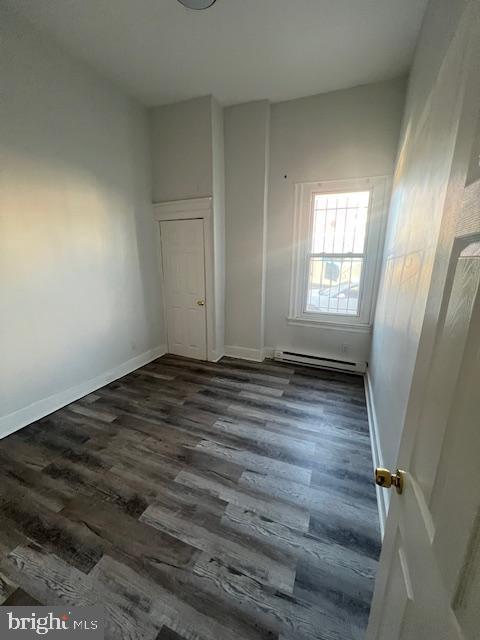 spare room featuring baseboard heating and dark hardwood / wood-style flooring