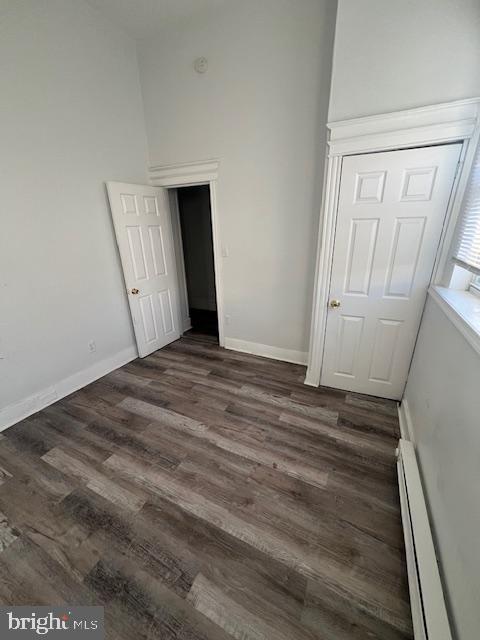 unfurnished bedroom featuring dark hardwood / wood-style floors, a baseboard heating unit, and a closet