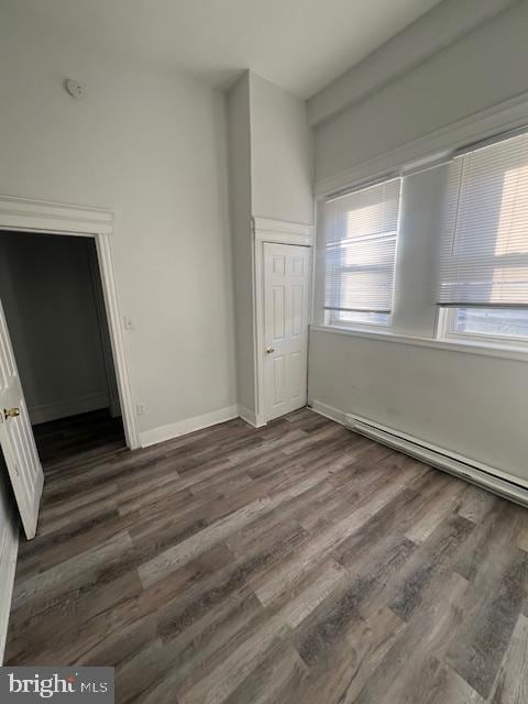 unfurnished bedroom with baseboard heating, a closet, and dark hardwood / wood-style floors