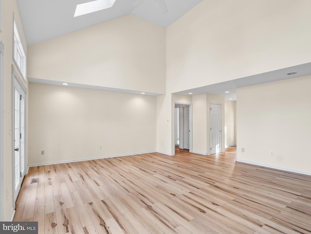 unfurnished living room with high vaulted ceiling, a skylight, ceiling fan, and light wood-type flooring