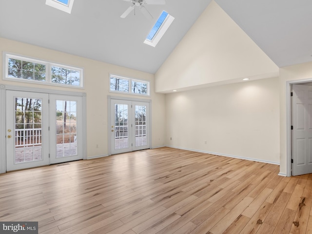 unfurnished living room with a skylight, high vaulted ceiling, ceiling fan, and light hardwood / wood-style flooring