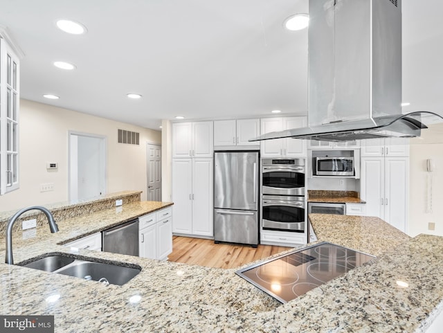 kitchen with island range hood, stainless steel appliances, light stone counters, sink, and white cabinetry