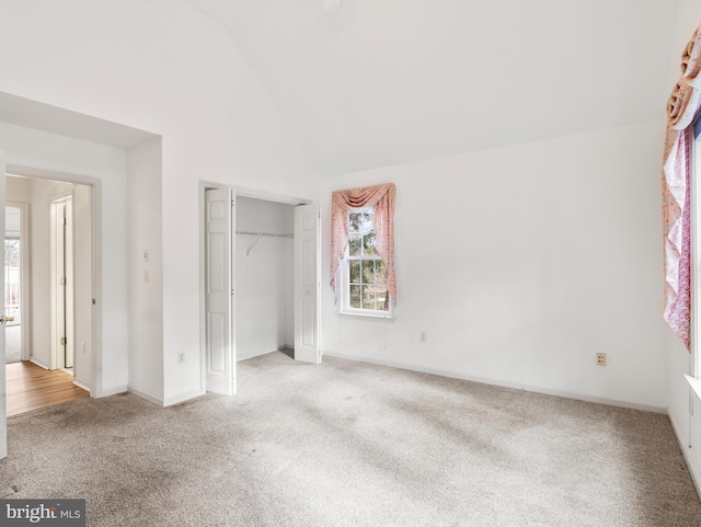 unfurnished bedroom featuring high vaulted ceiling, light colored carpet, and a closet